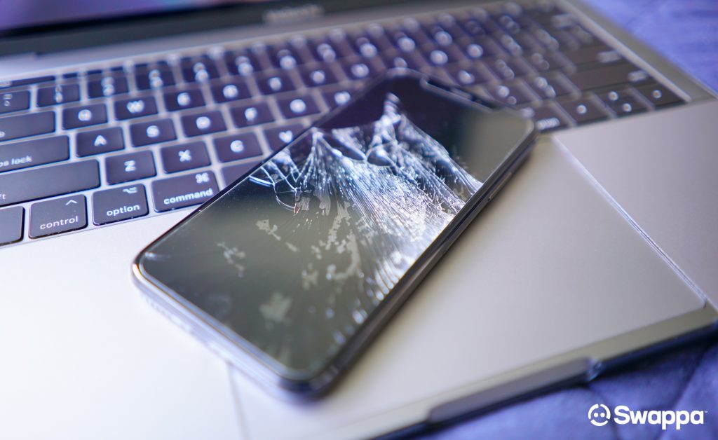 Broken iPhone X screen on top of MacBook Pro 13-inch